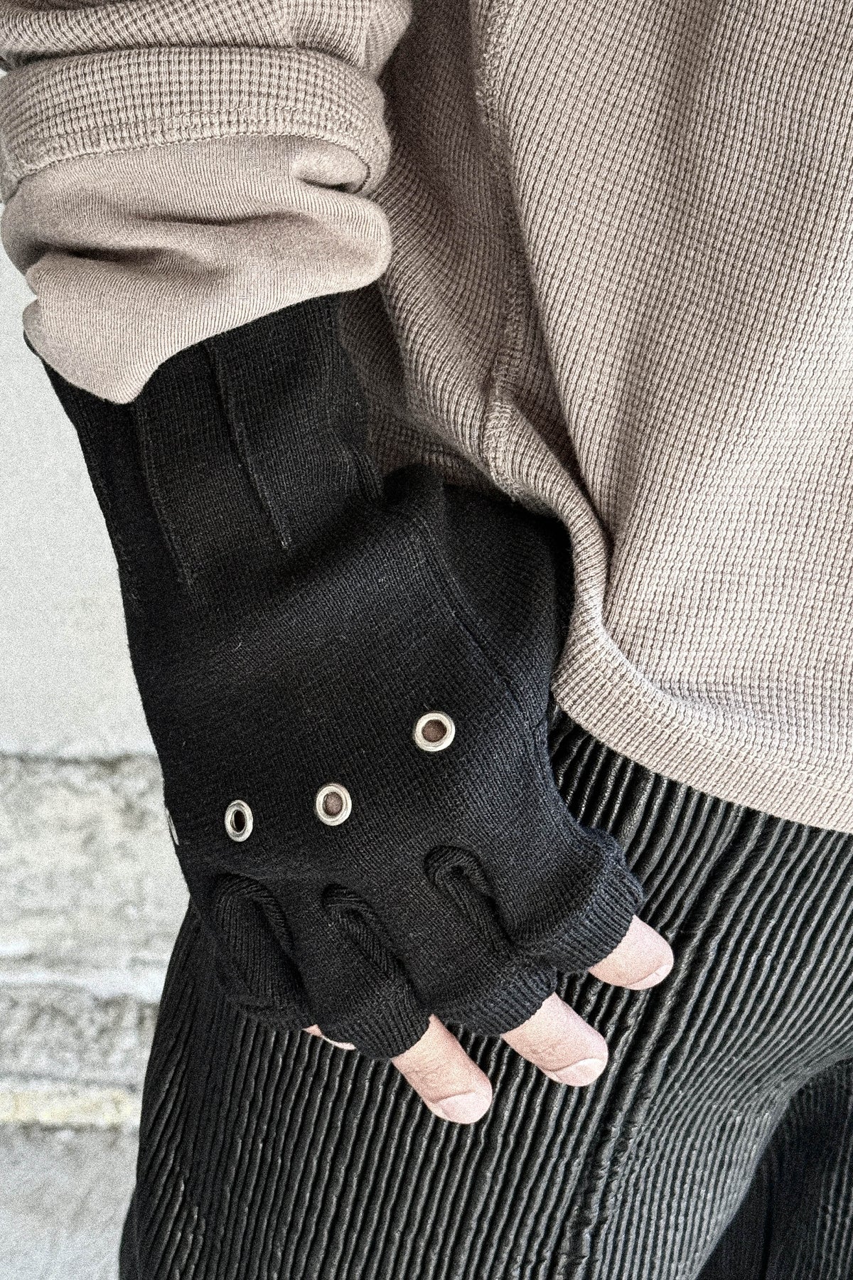 Hand resting at the hip wearing the Ākhira Rib Glove, showing metal knuckle eyelets and fingerless cut