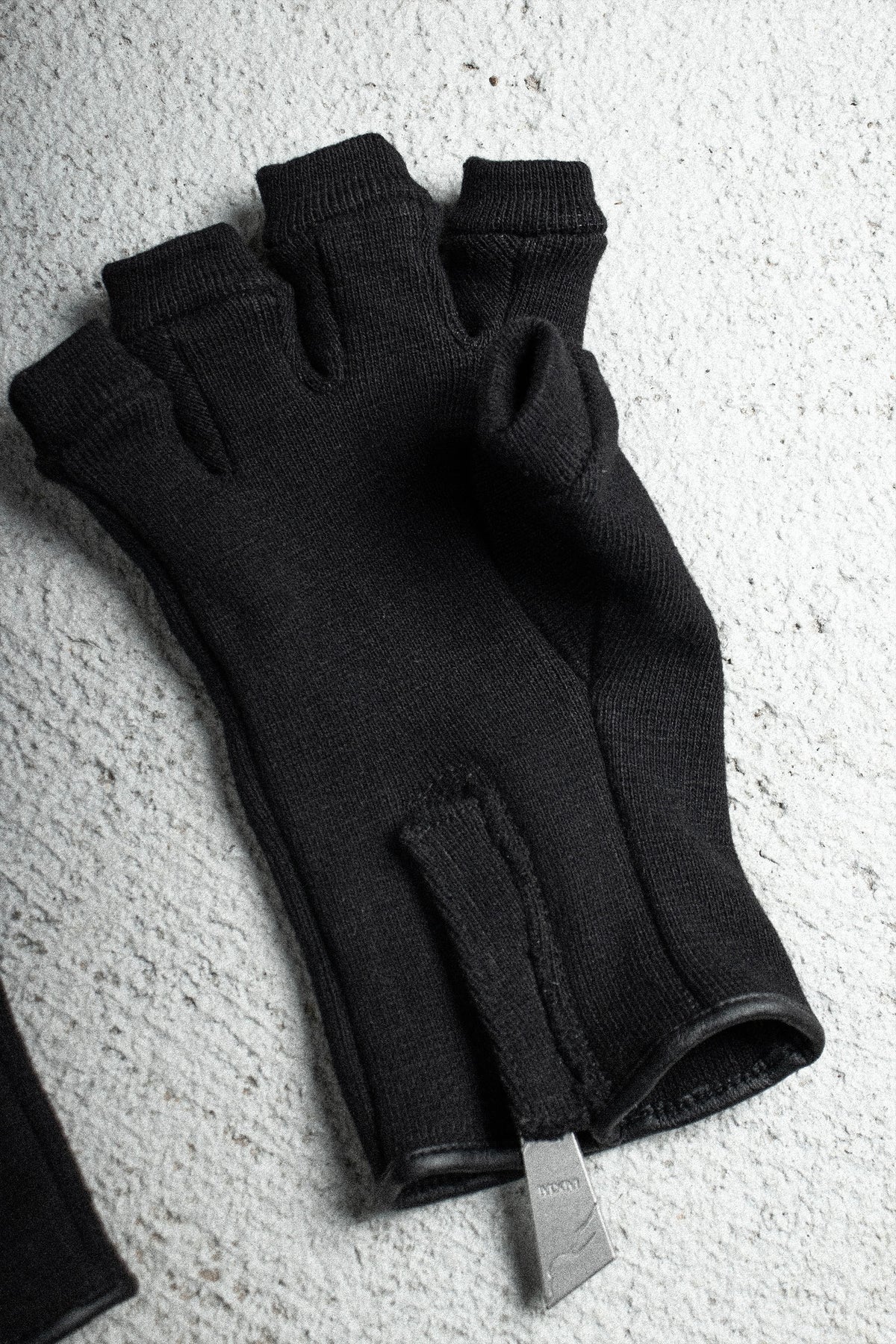 Ākhira Rib Glove laid flat on concrete, palm side with zipper pull at the wrist