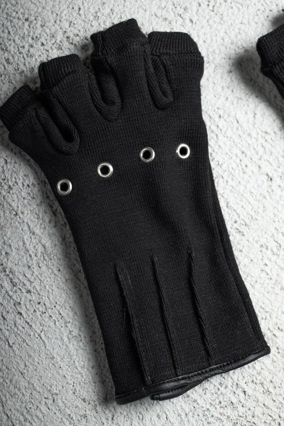 Ākhira Rib Glove laid flat on concrete, back of hand with four metal eyelets